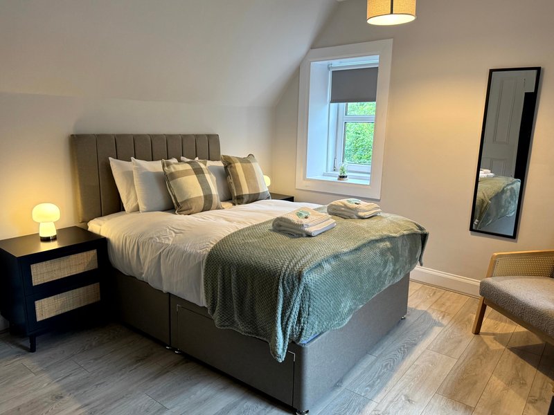 Modern bedroom with upholstered bed, white bedding, grey throw, pillows, bedside lamp and window