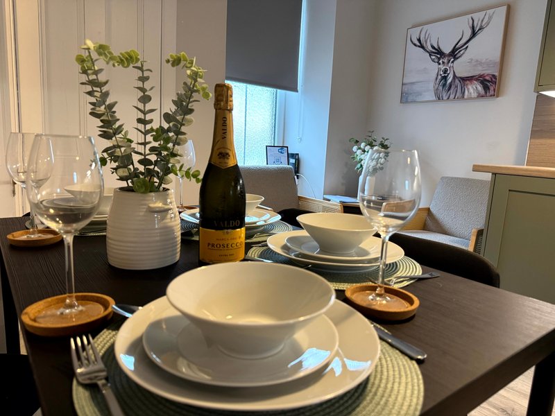 Formally set dining table with white plates, wine glasses, champagne bottle and fresh flowers