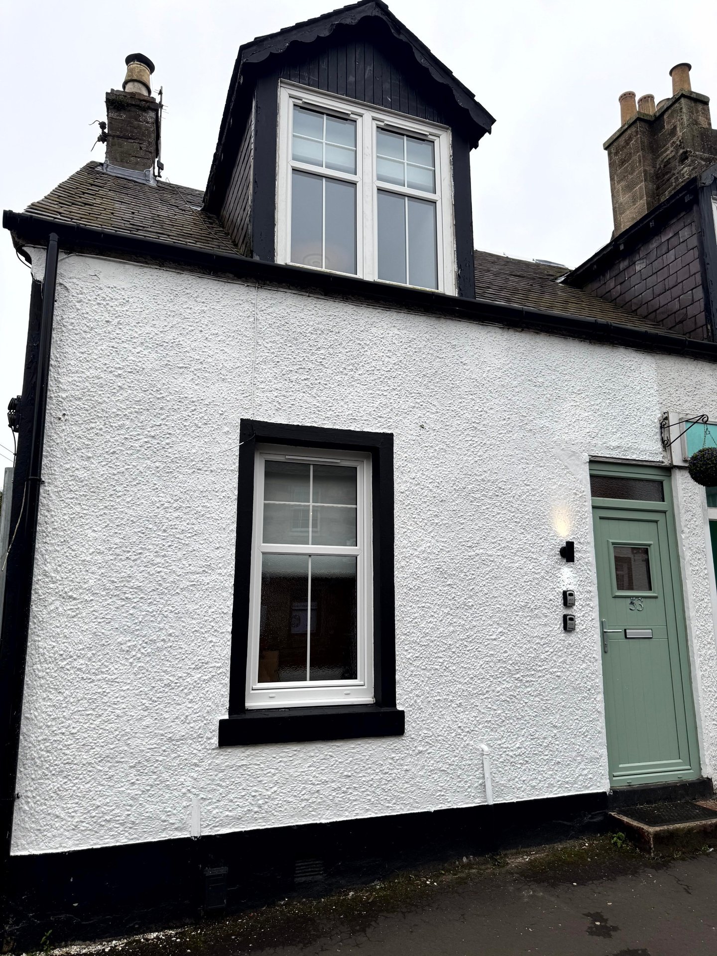 White and black cottage exterior with dormer window, green door and black-framed windows