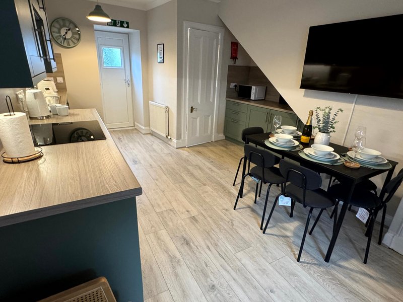 Open-plan kitchen and dining area with black table, wooden flooring and wall-mounted TV