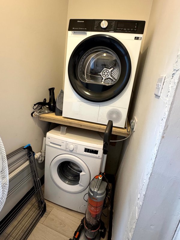 Stacked washer and dryer in utility room with wooden shelf and fire extinguisher