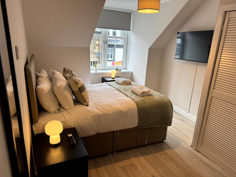 Modern bedroom with double bed, wooden floor, wall-mounted TV and window with city view