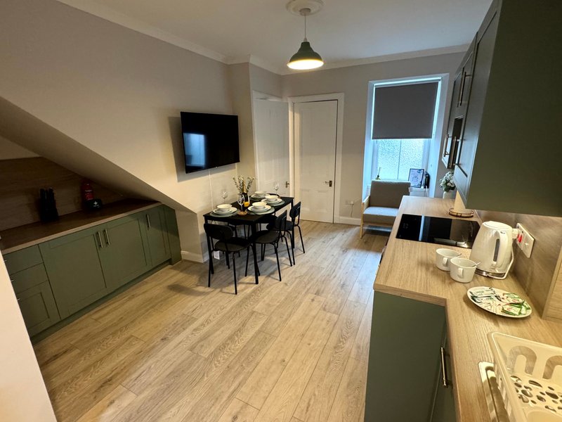 Open-plan kitchen and dining area with sage green cabinetry, wooden countertop, dining table and wall-mounted television
