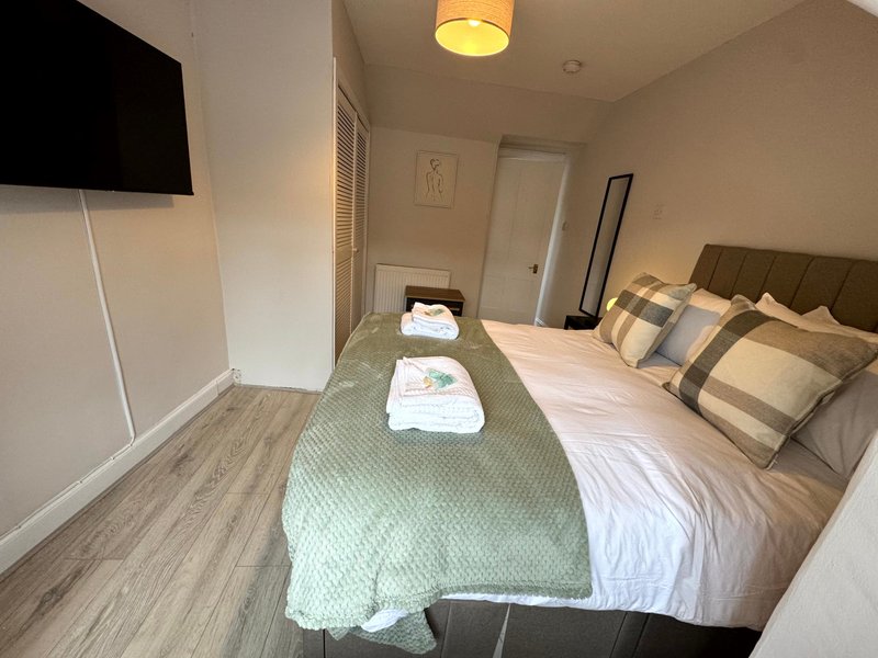 Modern bedroom with double bed, folded towels, TV, and wooden flooring