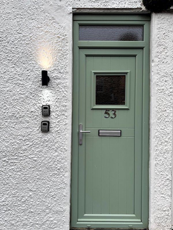 Green front door with window and house number 53 on white-rendered exterior wall
