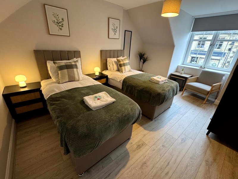 Twin bedroom with two single beds, wooden flooring, bedside lamps and window overlooking street