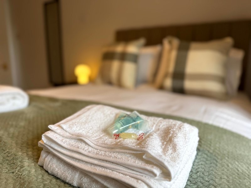 Bedroom with folded towels on bed, decorative cushions, and warm lighting