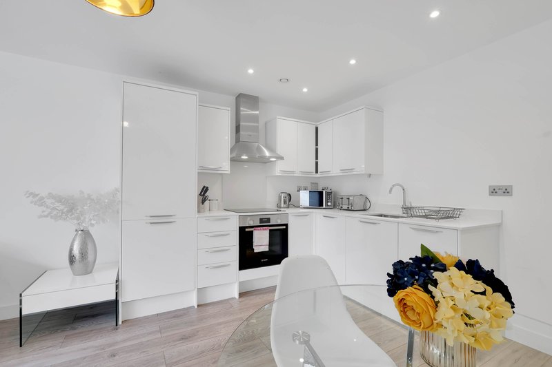Modern white kitchen with built-in appliances, island seating, and yellow flowers in vase