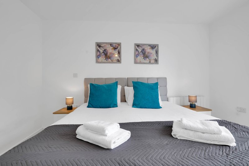 Modern bedroom with double bed, teal pillows, white bedding and framed wall art
