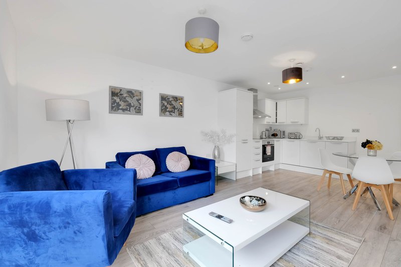 Open-plan living area with blue velvet sofa, white coffee table, and integrated kitchen with dining table
