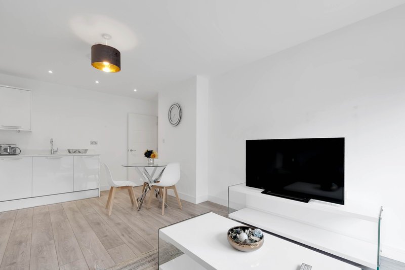 Modern open-plan living area with kitchen, dining table, TV and wooden flooring