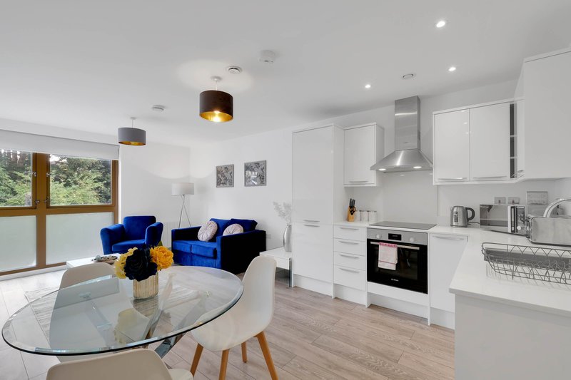 Open-plan kitchen and living area with white cabinetry, blue armchair, dining table and garden views