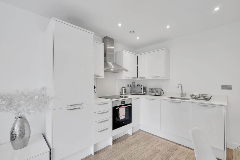 Modern white kitchen with built-in oven, range hood, wooden flooring and pendant lighting