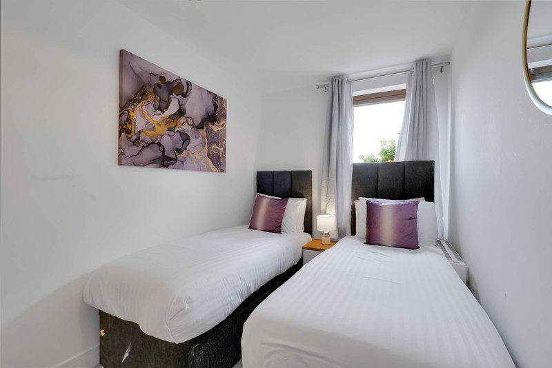 Twin bedroom with white bedding, purple cushions, framed artwork and window with grey curtains