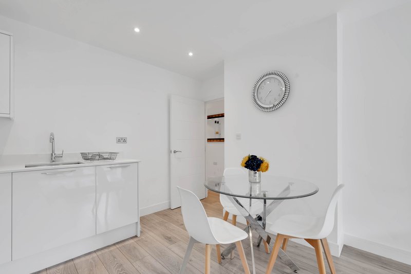 Modern open-plan kitchen and dining area with white cabinetry, glass table, and wooden flooring