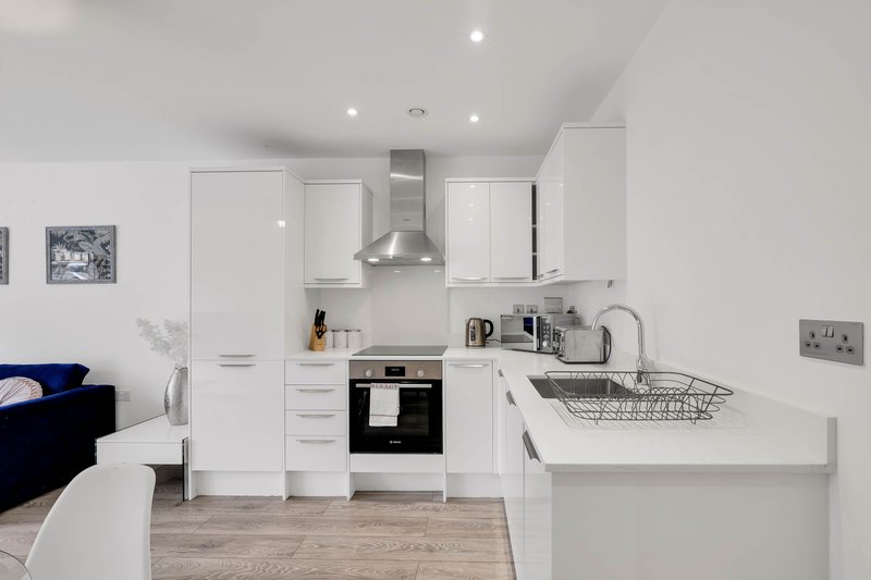 Modern white kitchen with integrated appliances, stainless steel extractor hood, and breakfast bar