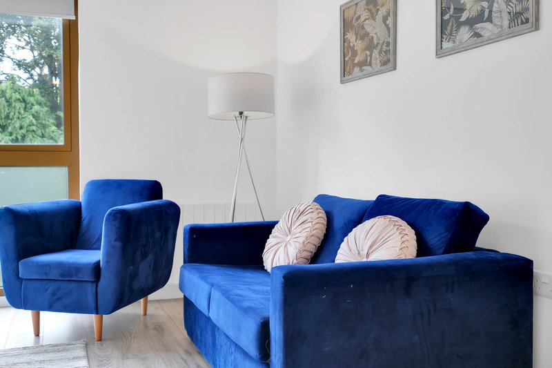 Modern living room with blue velvet sofa and armchair, floor lamp, decorative wall art