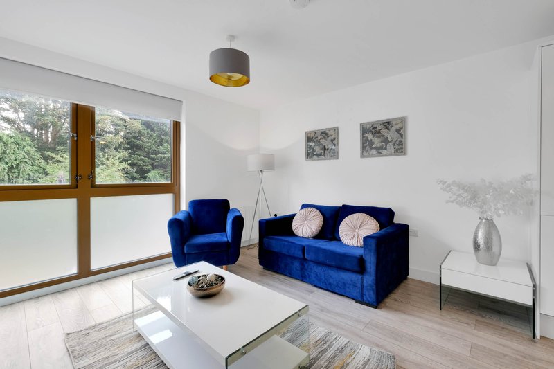 Modern living room with blue velvet sofa and armchair, white coffee table, wooden-framed windows and pendant light