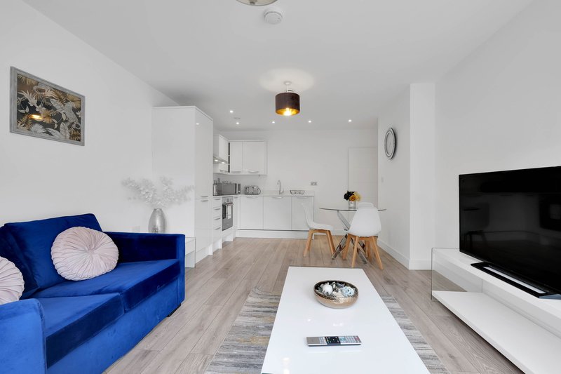 Modern open-plan living space with blue sofa, white kitchen, wooden flooring and TV unit