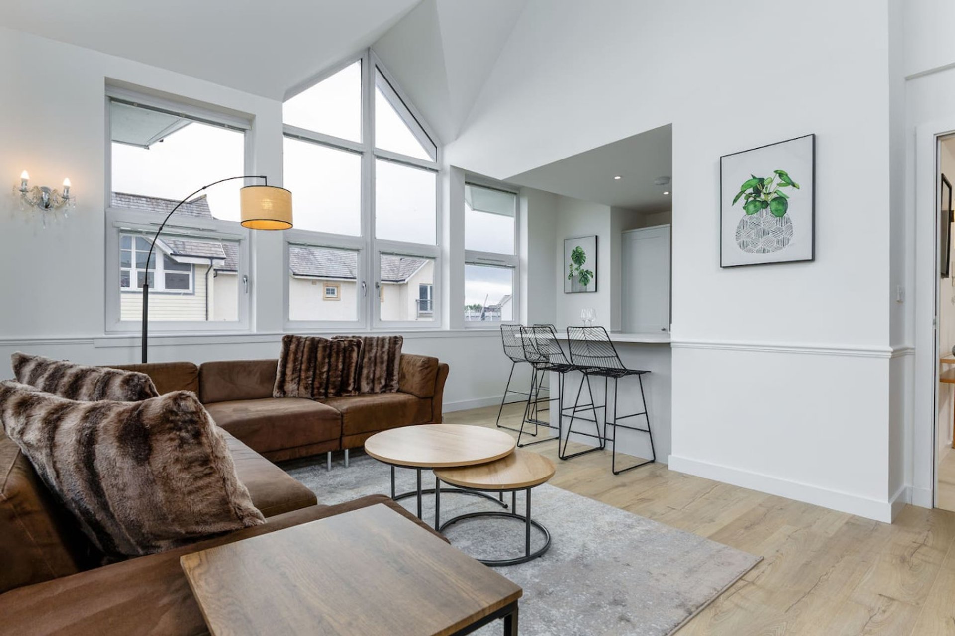 Open-plan living area with brown leather sofa, bar seating, wooden flooring and large windows