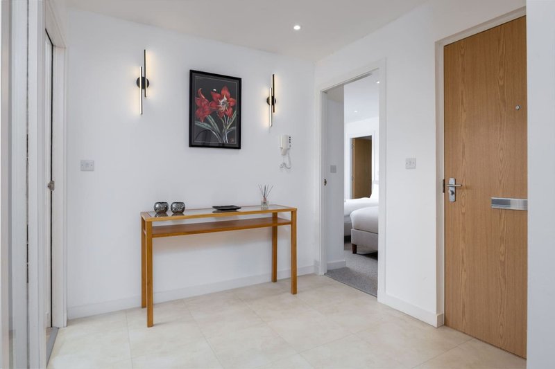 Modern entryway with wooden console table, framed floral artwork, wall sconces and light stone flooring