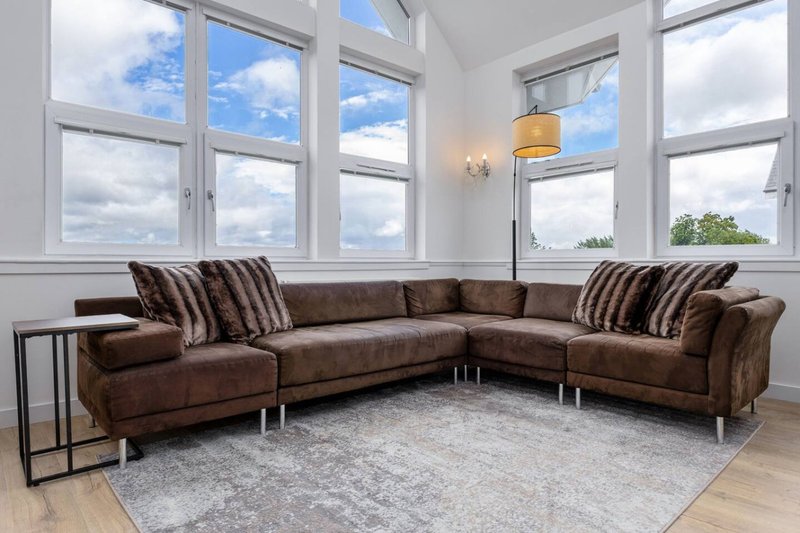 Bright living room with brown leather sectional sofa, striped cushions, large windows and pendant light