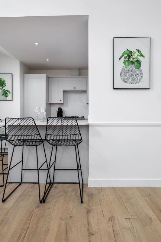 Modern open-plan kitchen and dining area with black bar stools and botanical wall art