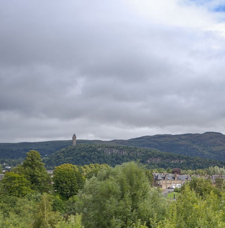 Scenic valley landscape with historic tower, forested hills, and stone buildings below