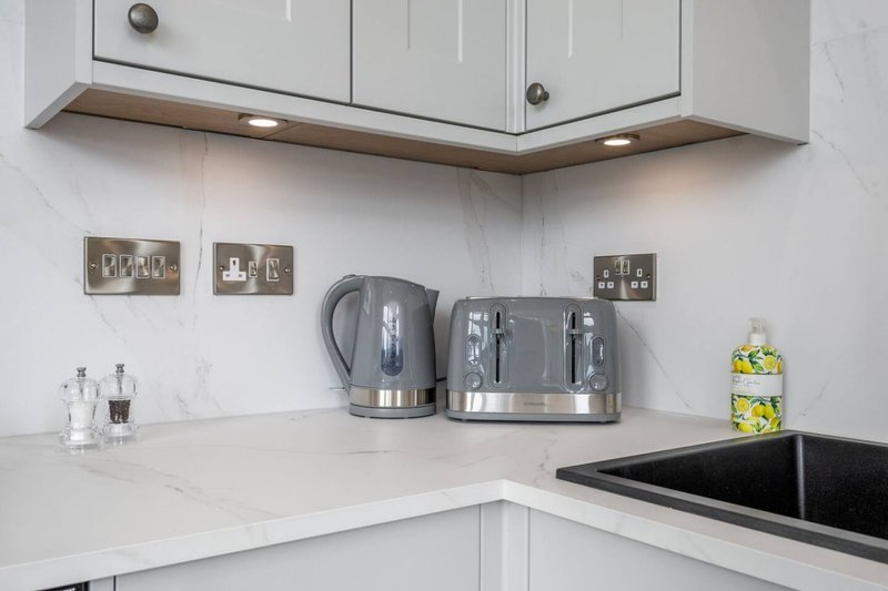 Modern white kitchen corner with kettle, toaster, and electrical outlets on marble countertop