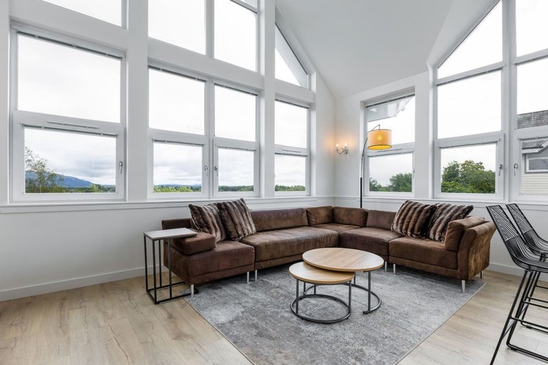 Bright corner lounge with brown sectional sofa, round coffee table, large windows and mountain views