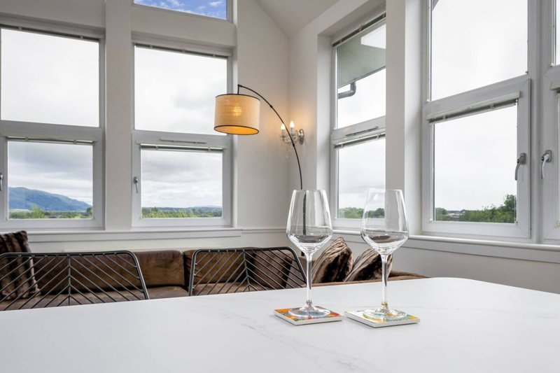 Bright dining area with large windows overlooking mountains, arc lamp, and table with wine glasses