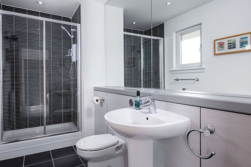 Modern bathroom with shower enclosure, pedestal sink, toilet, and window