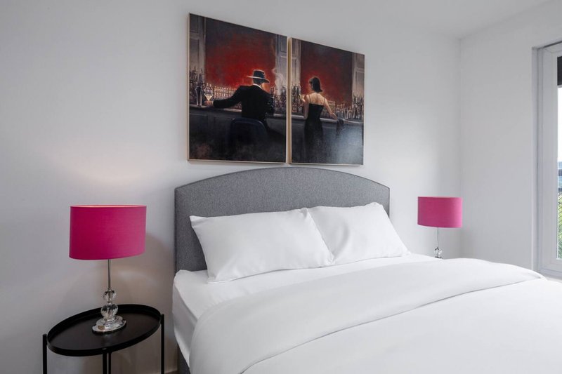 Modern bedroom with grey upholstered headboard, white bedding, pink bedside lamps and wall art