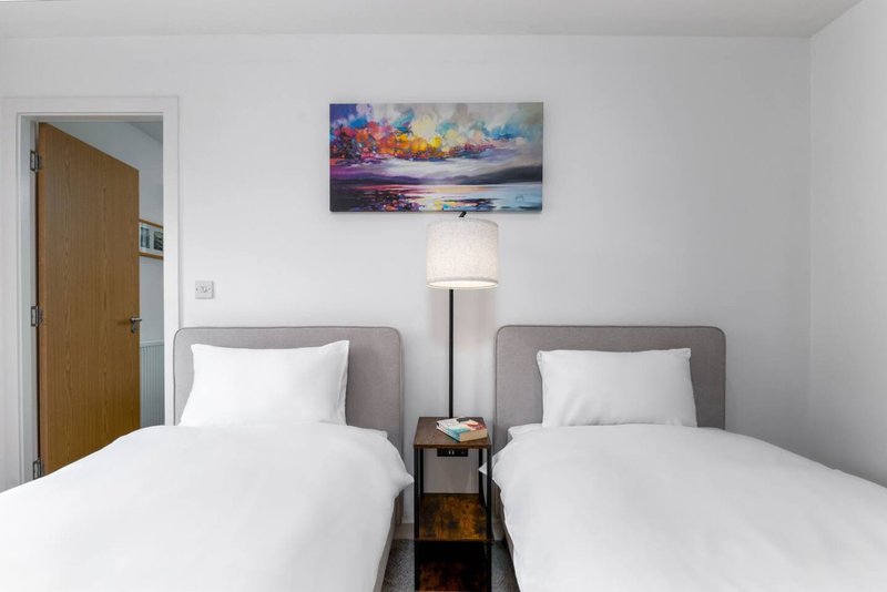Twin bedroom with two single beds, shared nightstand, lamp, and landscape artwork