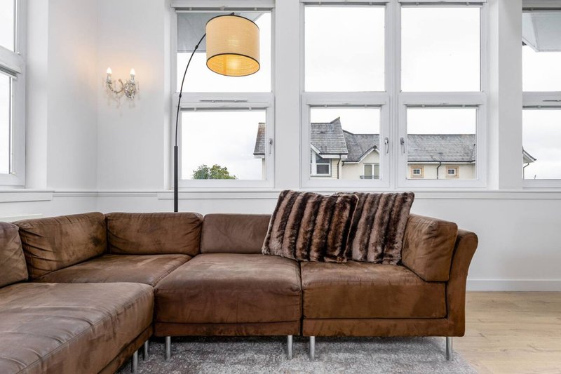 Modern living room with brown leather sectional sofa, striped cushion, arc floor lamp and large windows overlooking street