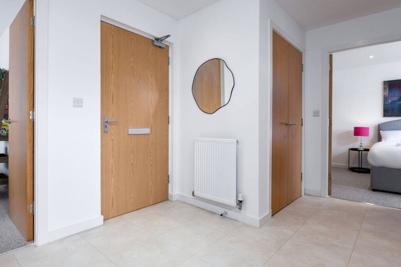 Bright hallway with wooden doors, round mirror, radiator and tiled flooring