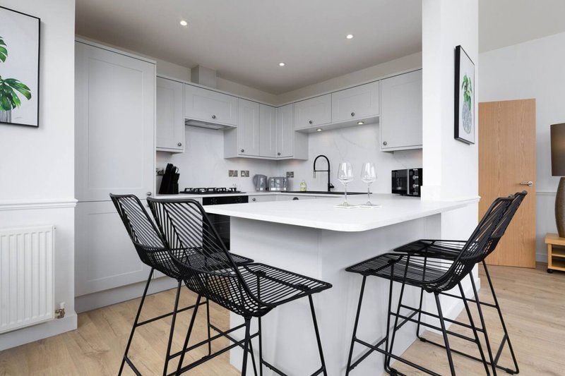 Modern white kitchen with island, black bar stools, and wooden flooring