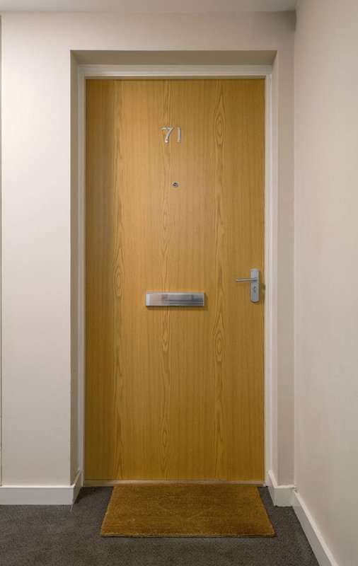 Wooden apartment door numbered 71 with mailslot and door handle