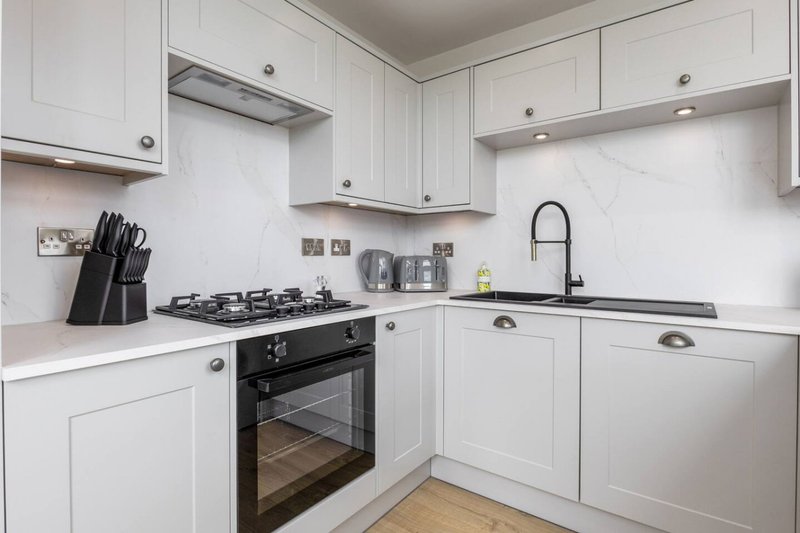 Modern white kitchen with black gas range, sink, and stainless steel appliances