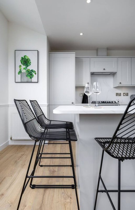 Modern kitchen with white cabinetry, island counter, black bar stools and wooden flooring