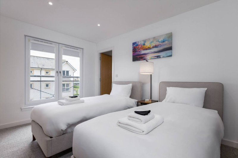 Twin bedroom with two single beds, grey headboards, and window overlooking residential street