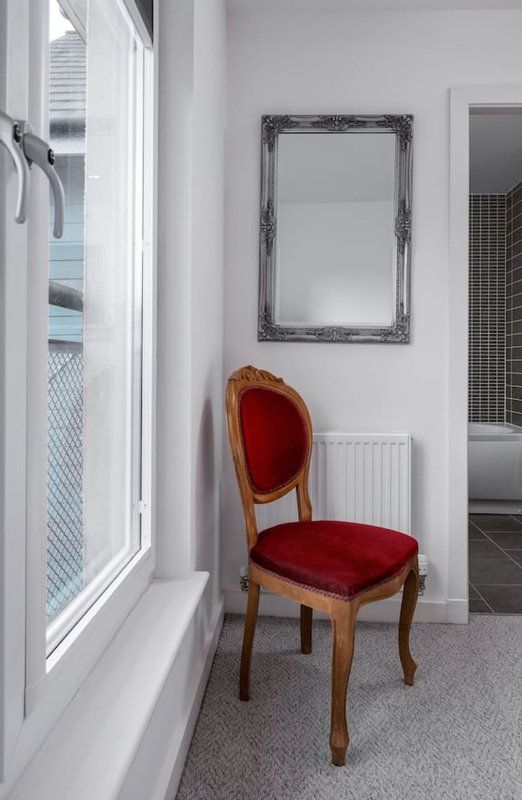 Modern hallway with red velvet chair, mirror, and bright window with shutters