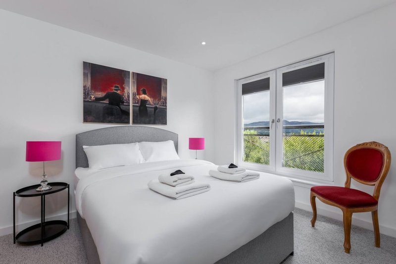 Modern bedroom with double bed, pink bedside lamps, artwork above headboard, and countryside view