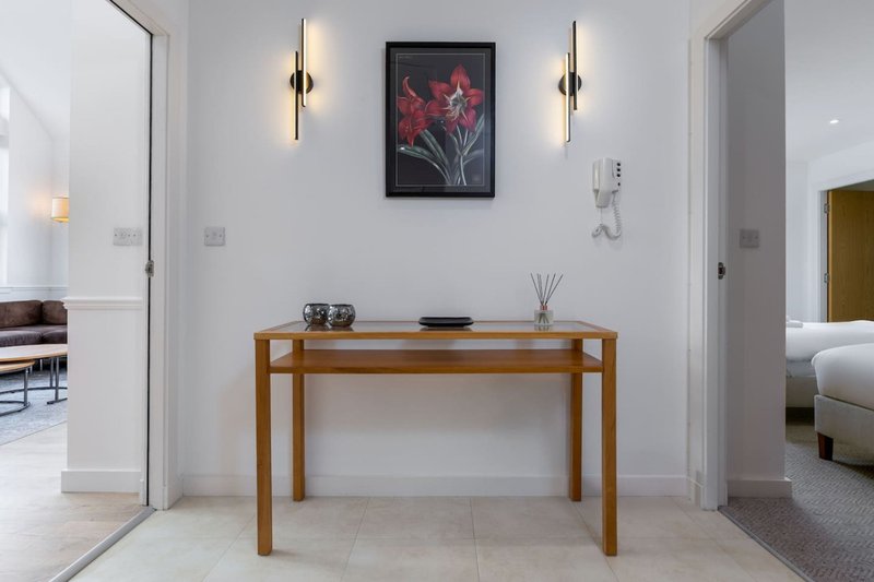 Modern hallway with wooden console table, framed floral artwork, and brass wall sconces