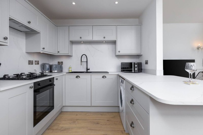 Modern kitchen with white cabinetry, black appliances, wooden flooring and island counter