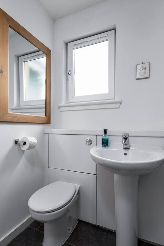 Clean modern bathroom with pedestal sink, toilet, mirror and window