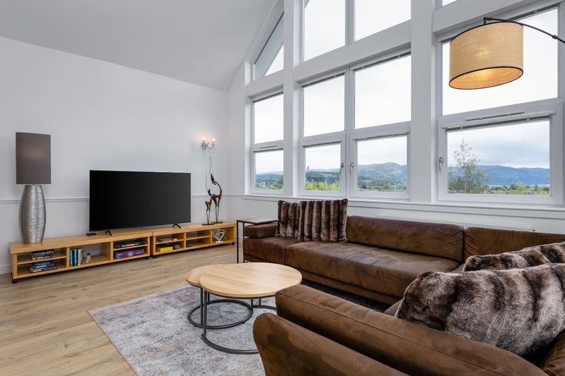 Modern living room with brown leather sofa, wooden TV unit, round coffee table and mountain views