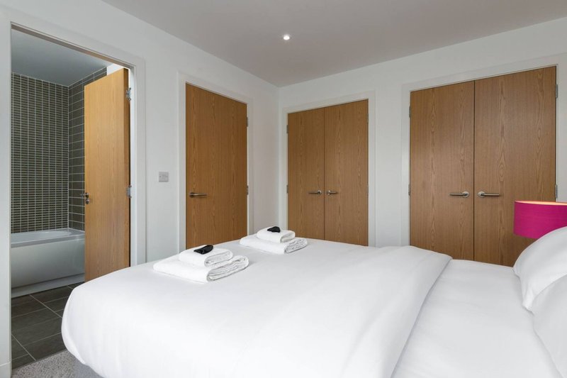 Modern bedroom with two double beds, wooden doors, ensuite bathroom and pink headboard detail