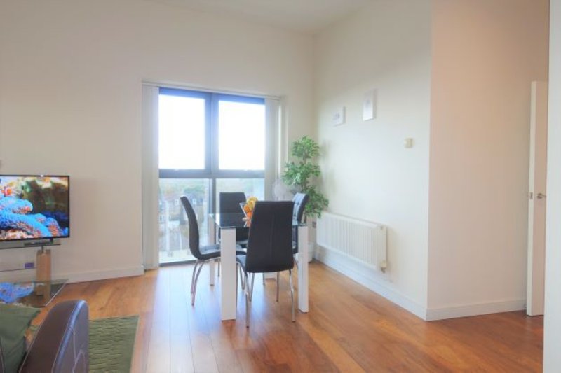 Open-plan living space with wooden flooring, dining table, black chair, and glass doors to balcony