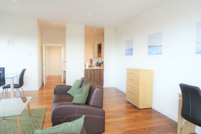 Open-plan living area with brown sofa, wooden flooring, kitchenette, and modern furnishings